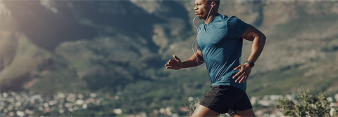 Biohacking und Spotler: Ein sportlicher Mann in blauer Laufkleidung joggt mit Kopfhörern durch eine bergige Landschaft. Symbol für Fitness, Leistungssteigerung und natürliche Regeneration durch gezielte Ernährung und Supplements.