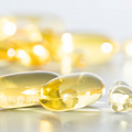 Nahaufnahme von goldgelben Omega-3-Kapseln auf einer reflektierenden Oberfläche. Die weichen, glänzenden Kapseln liegen dicht beieinander.